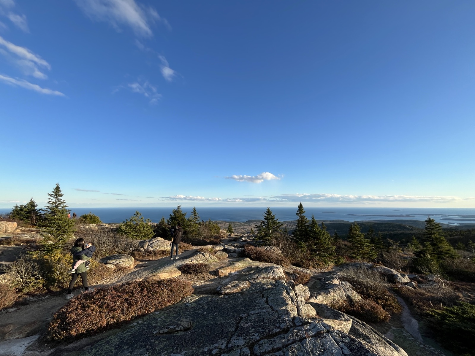 Family hiking the granite summit of Cadillac Mountain, Acadia National Park, with the Atlantic and offshore islands beyond