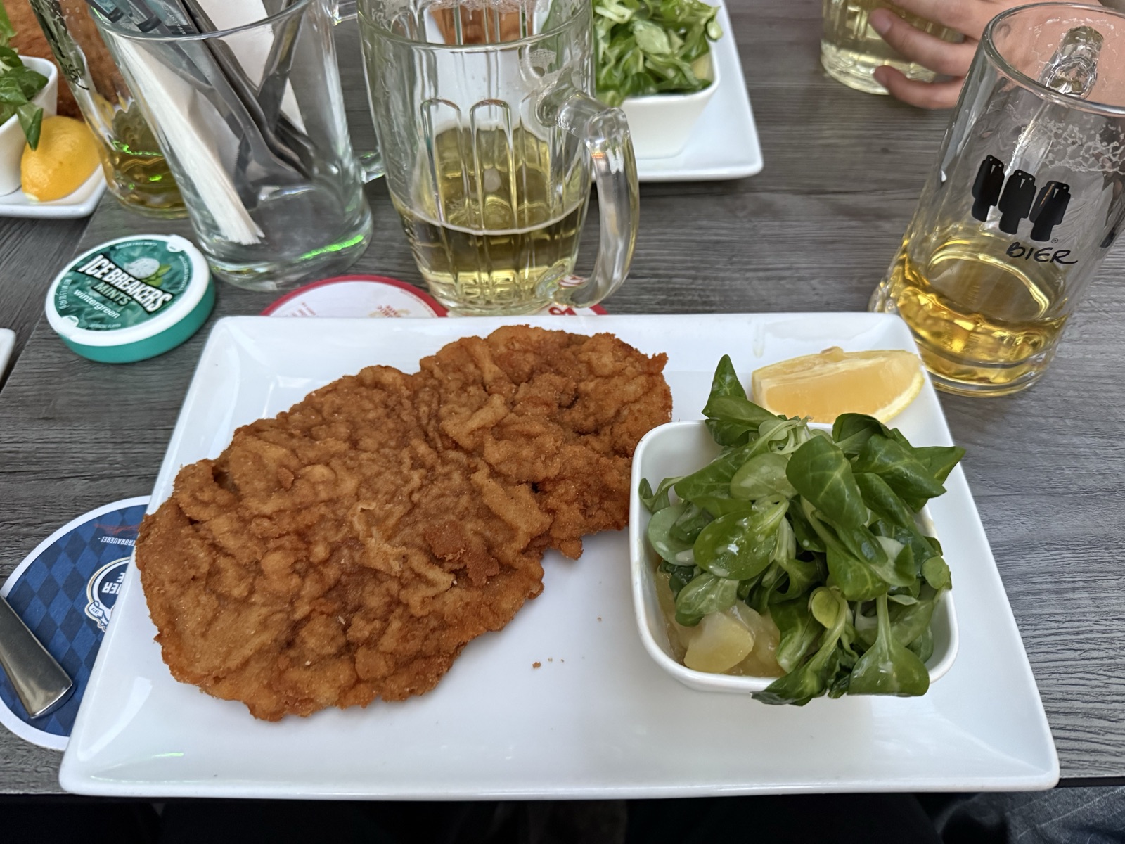 Wiener Schnitzel with a lemon wedge and lamb's lettuce salad, beer in the background